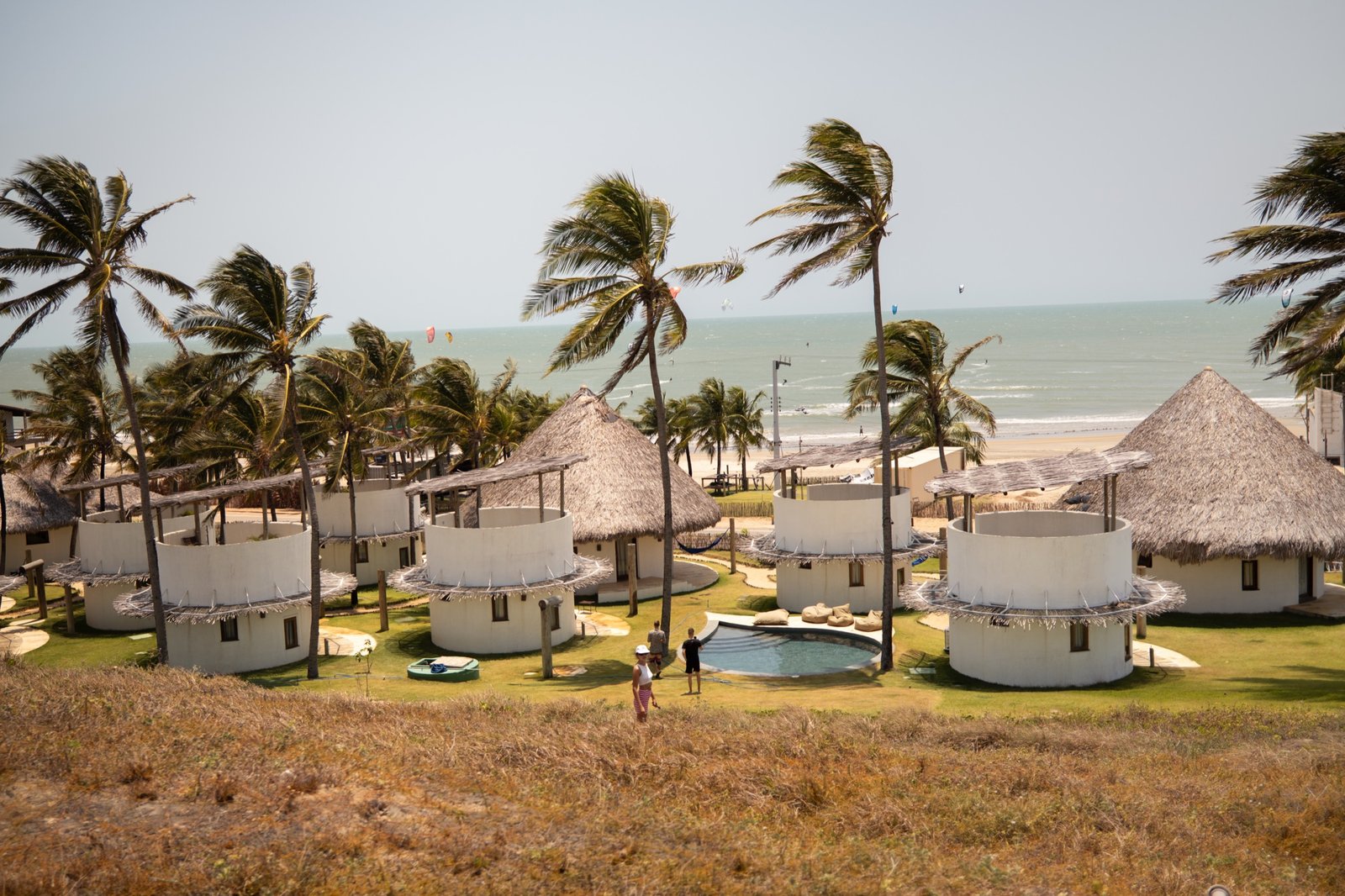 Round bungalows of the VentoVinte boutique hotel among palms at golden hour, the ocean behind