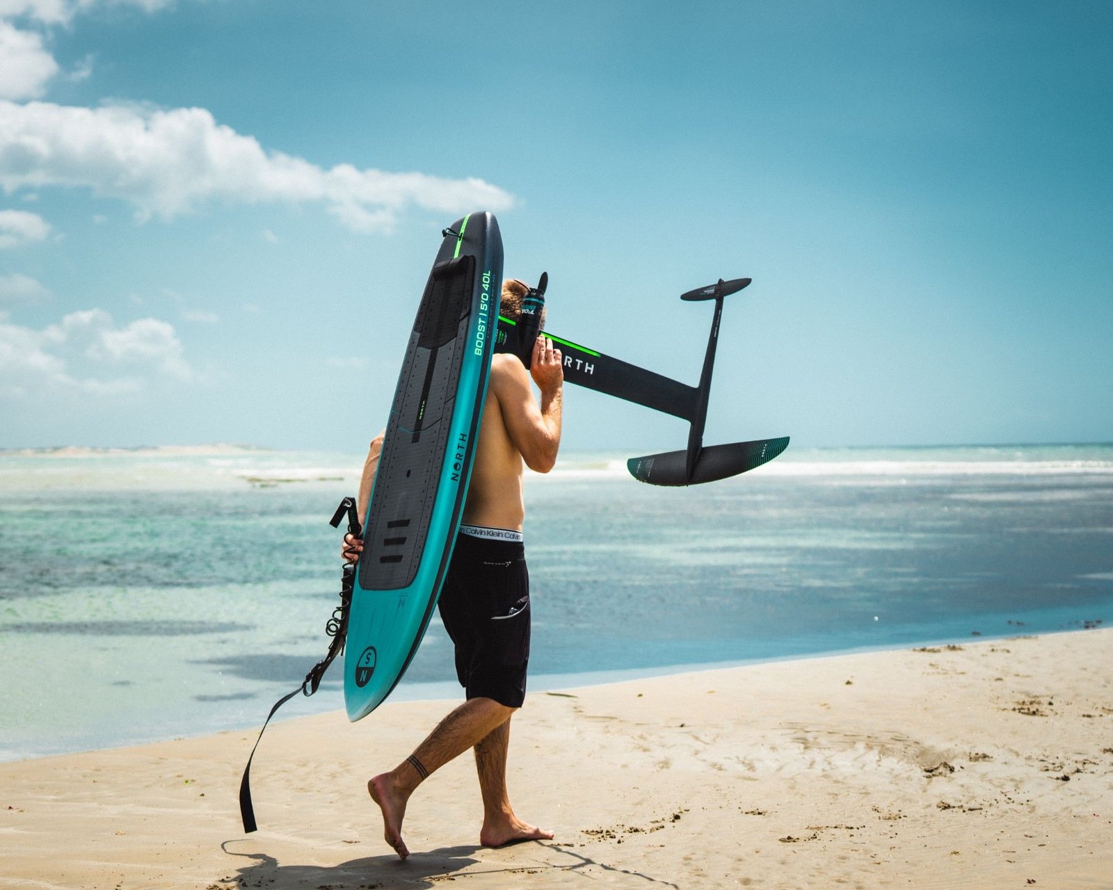 Rider carrying a North foilboard along the shoreline on a glassy zero-wind day