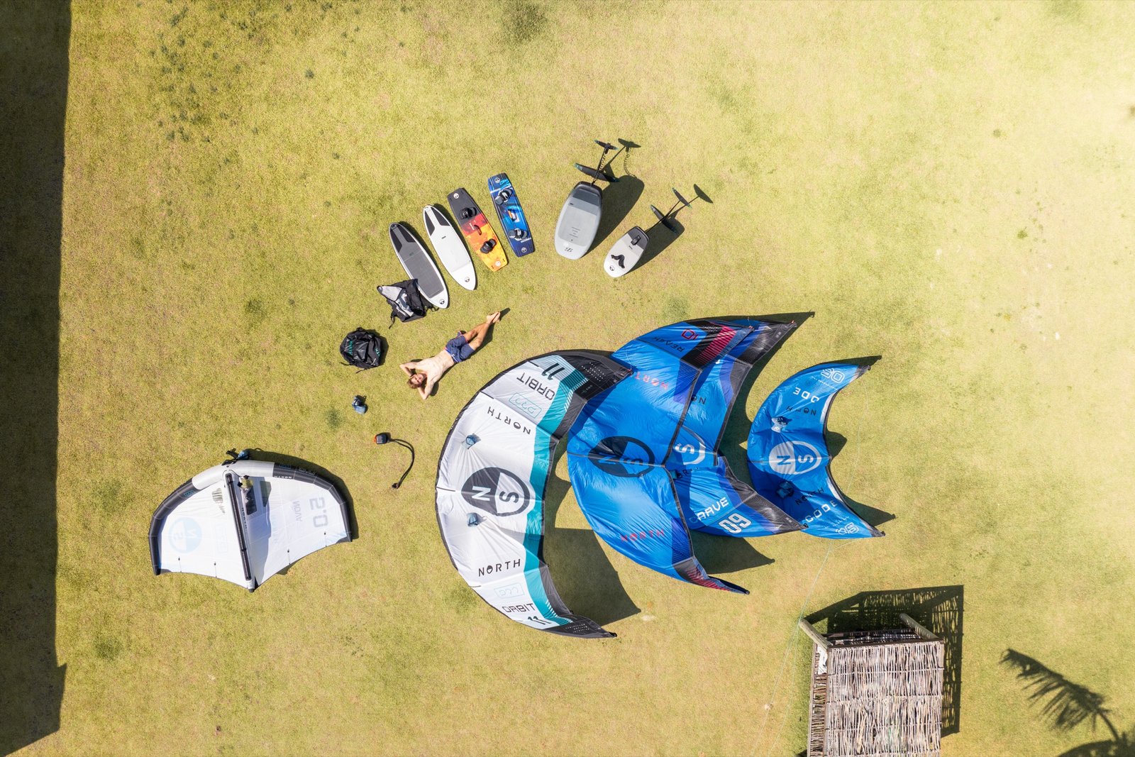 Aerial flat-lay of a full North kite quiver, boards and harnesses laid out on grass