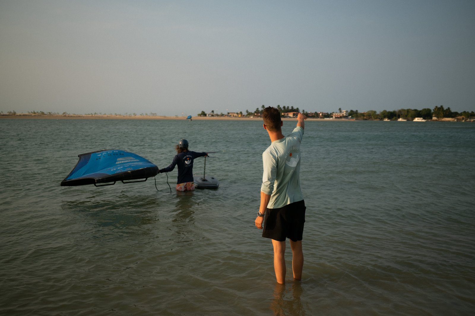 Wingfoiler crossing flat water at the Mundau lagoon while a student watches from the shallows